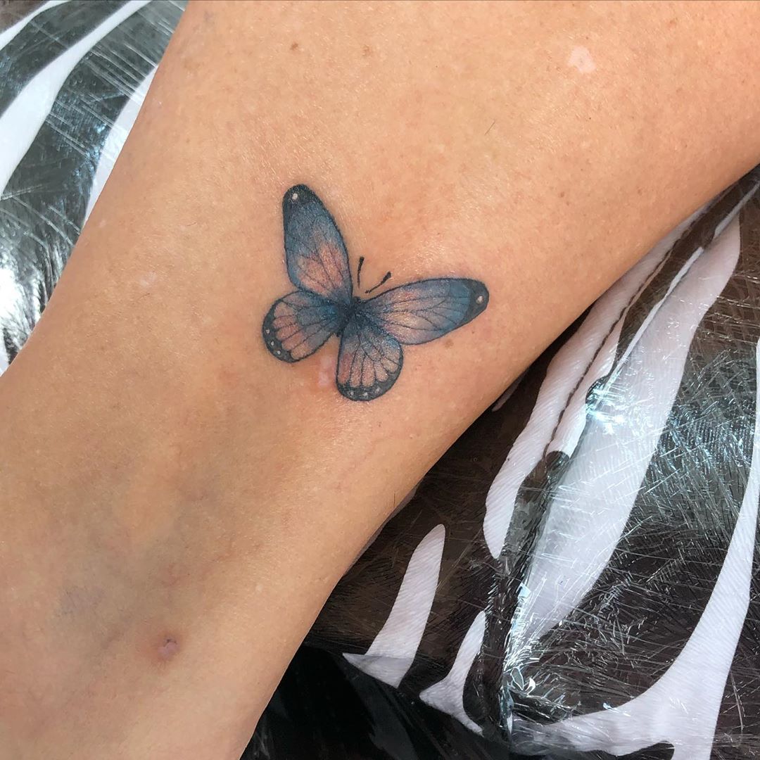small color tattoo on woman's lower leg of a delicate realistic blue butterfly