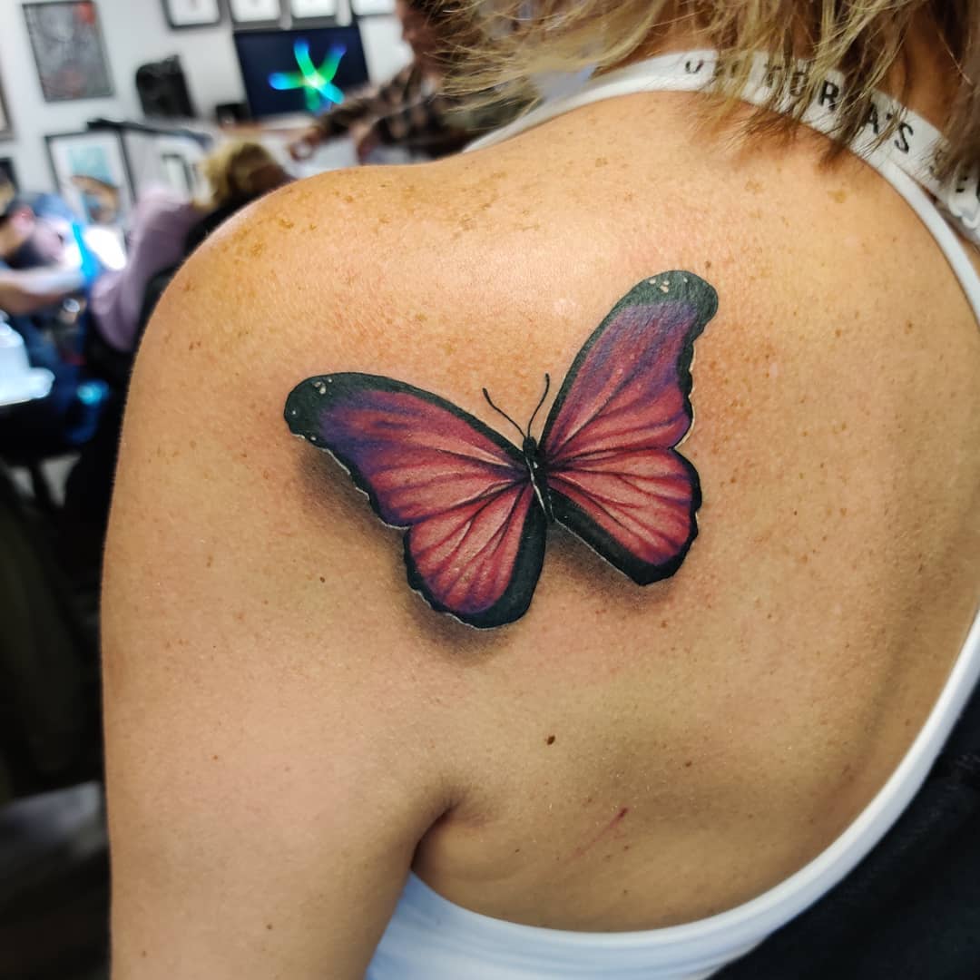 large color tattoo on woman's shoulder of realistic pink butterfly with shadow