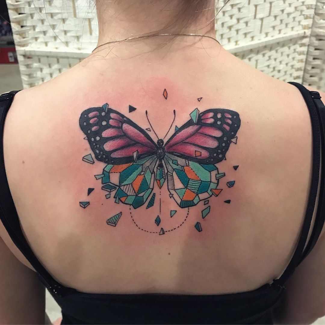 large color geometric tattoo on a woman's upper back of surrealistic butterfly with bottom half made of shattering crystals