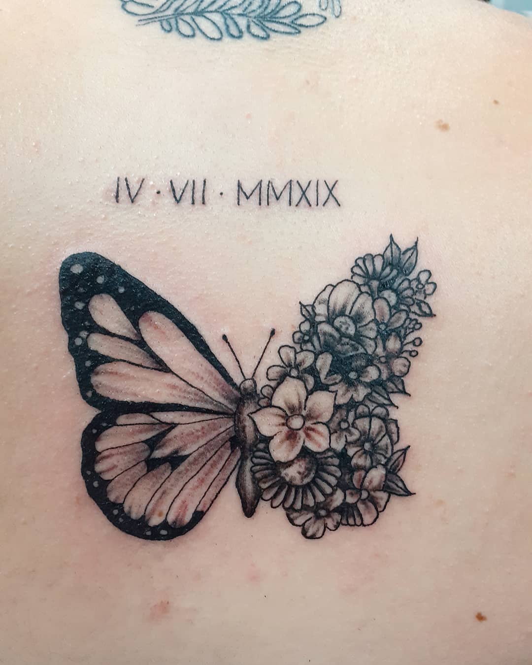 medium-sized black and grey tattoo on woman's upper back of butterfly with one floral wing