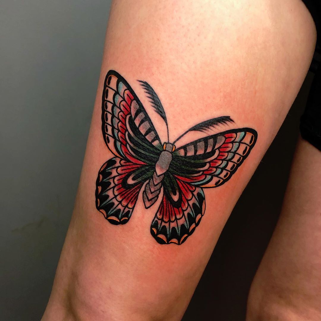 large color tattoo on thigh of a traditional blue and red butterfly