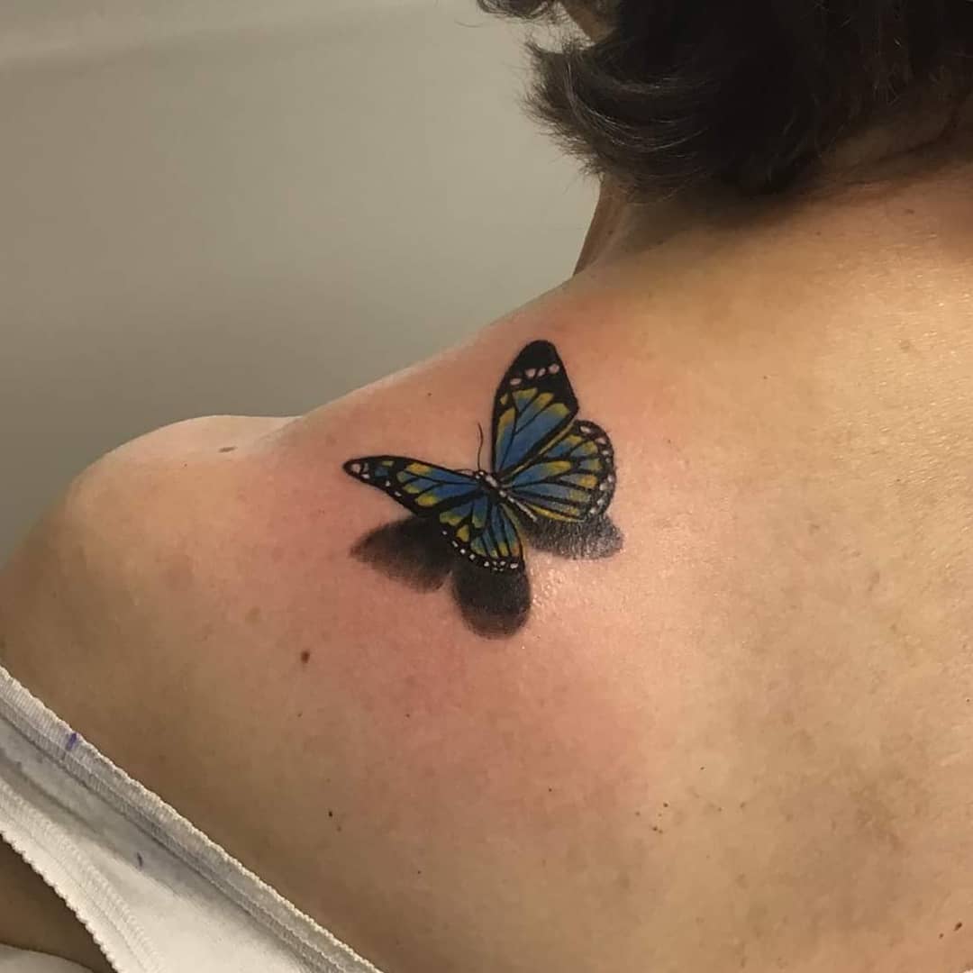 medium-sized color 3d tattoo on woman's shoulder of realistic blue butterfly with shadow