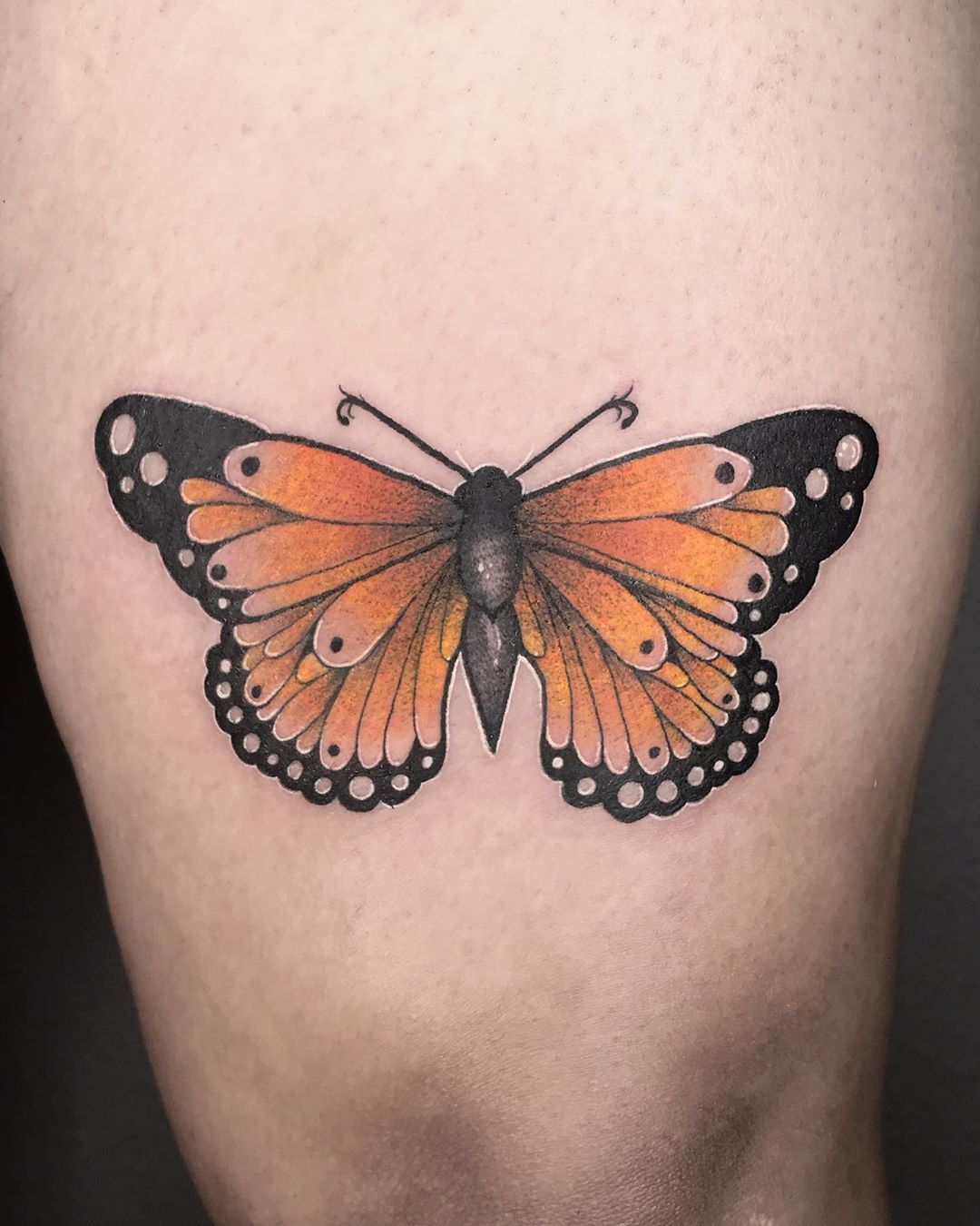 medium-sized color tattoo on woman's thigh of orange realistic butterfly