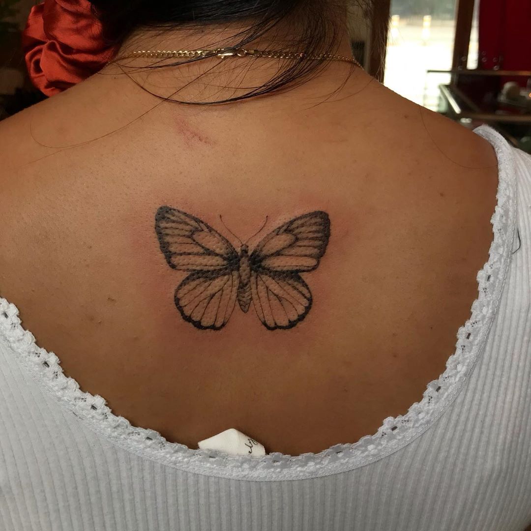 medium-sized black and grey tattoo on woman's upper backof realistic butterfly