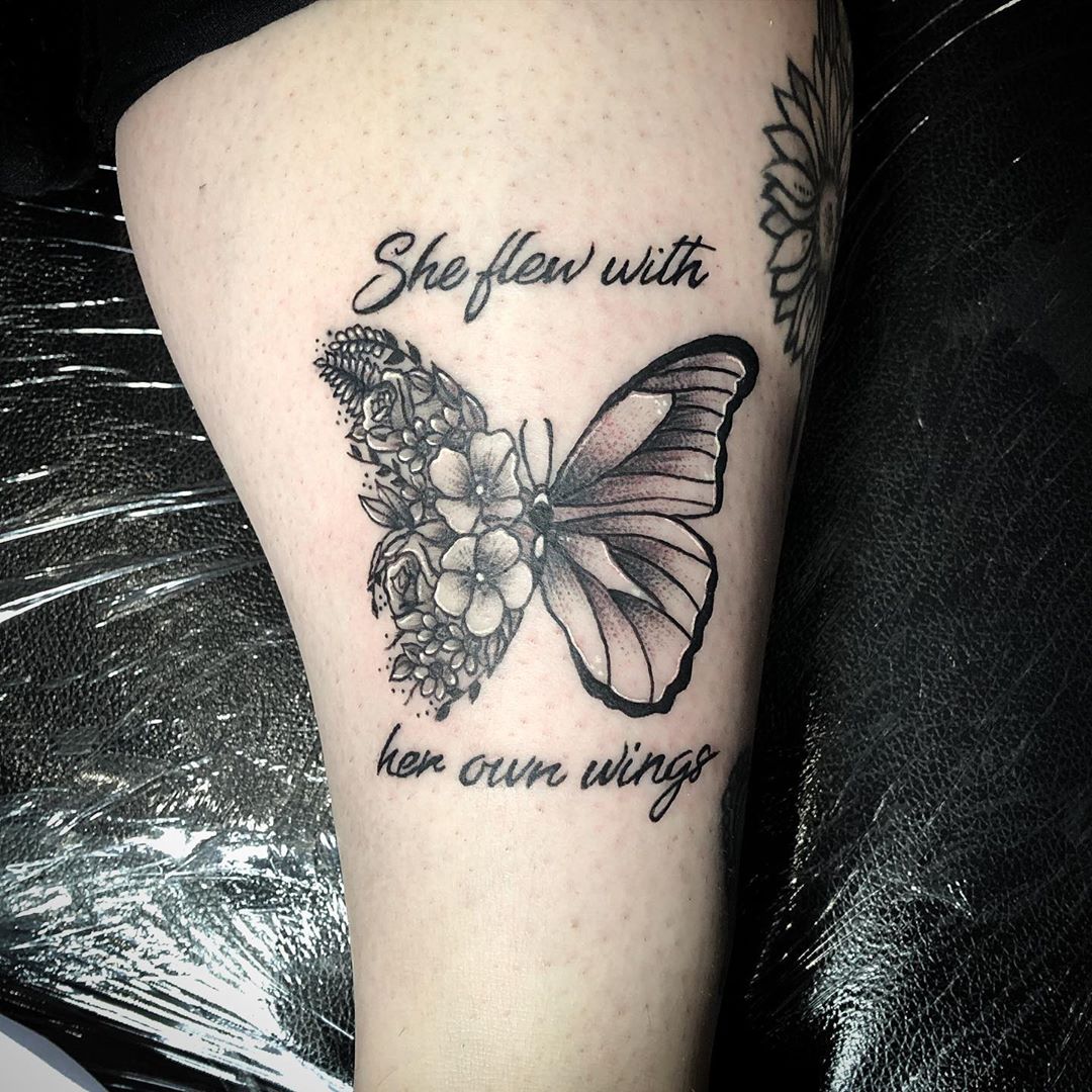 large black and grey tattoo on woman's thigh of butterfly with one floral wing and quote