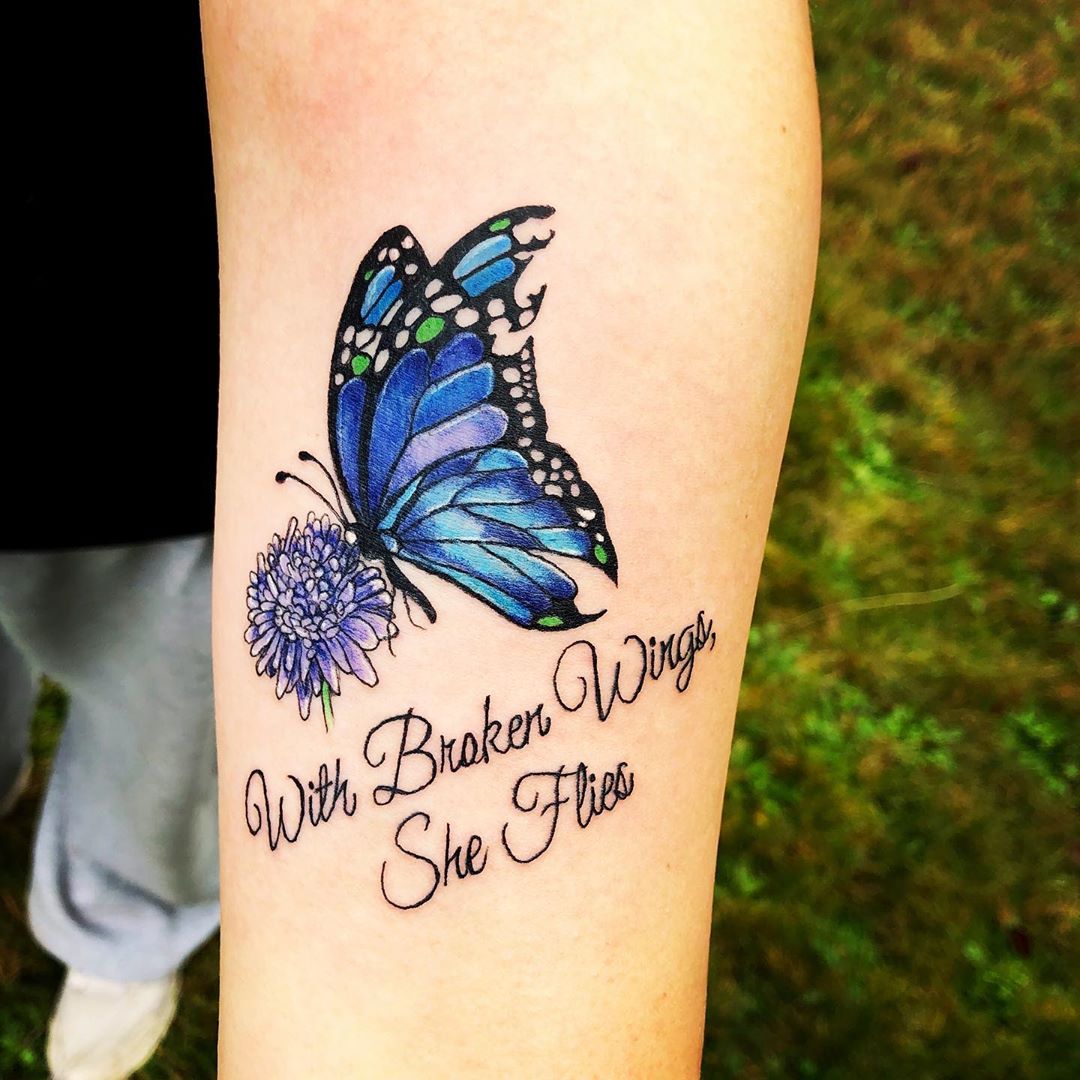 medium-sized color tattoo on woman's forearm of blue and purple butterfly with flower and quote