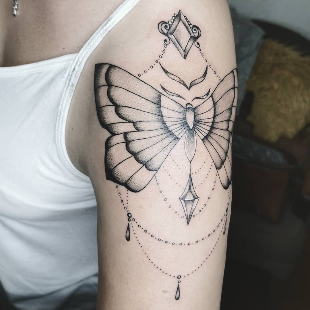 large black and grey tattoo on woman's upper arm of ornamental butterfly