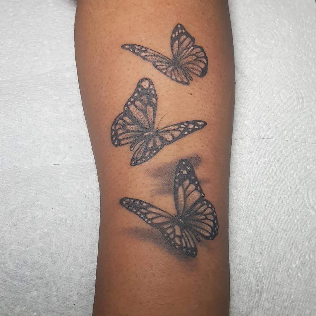 large black and grey tattoos on woman's lower leg of three realistic butterflies flying with shadow