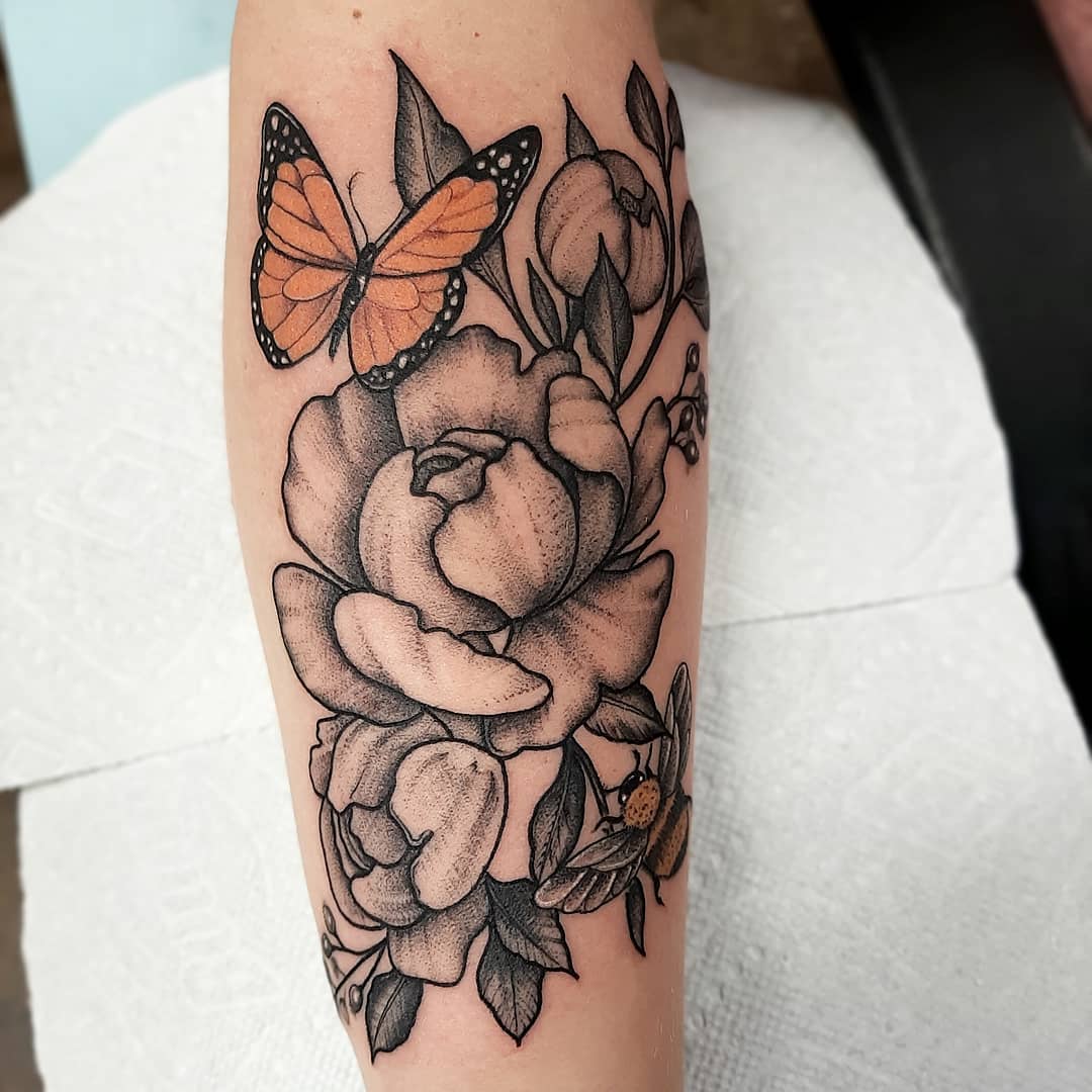 large black and color tattoo on lower leg of a bouquet of roses with an orange butterfly and bumble bee