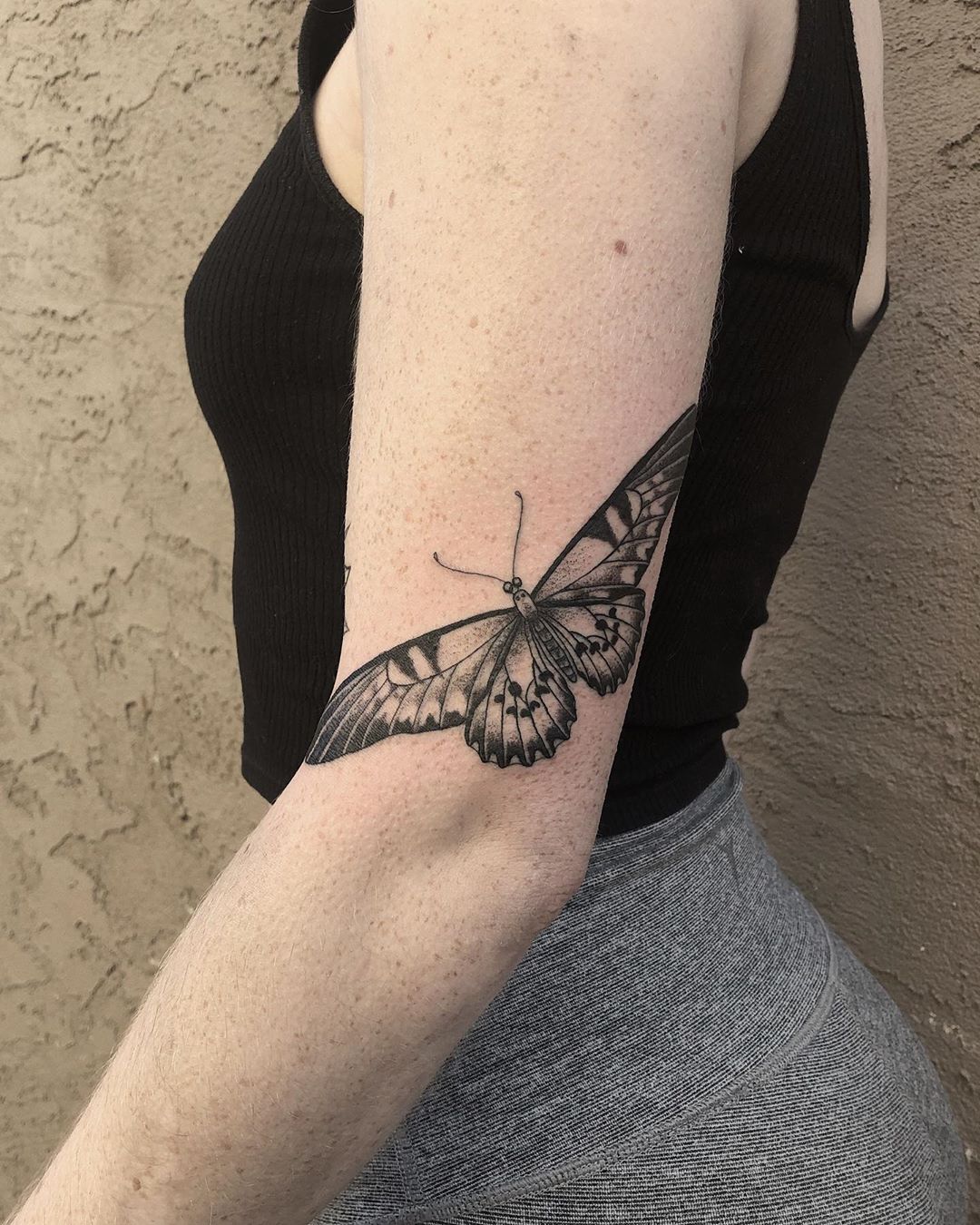 medium-sized black and grey tattoo on back of woman's upper arm of realistic butterfly