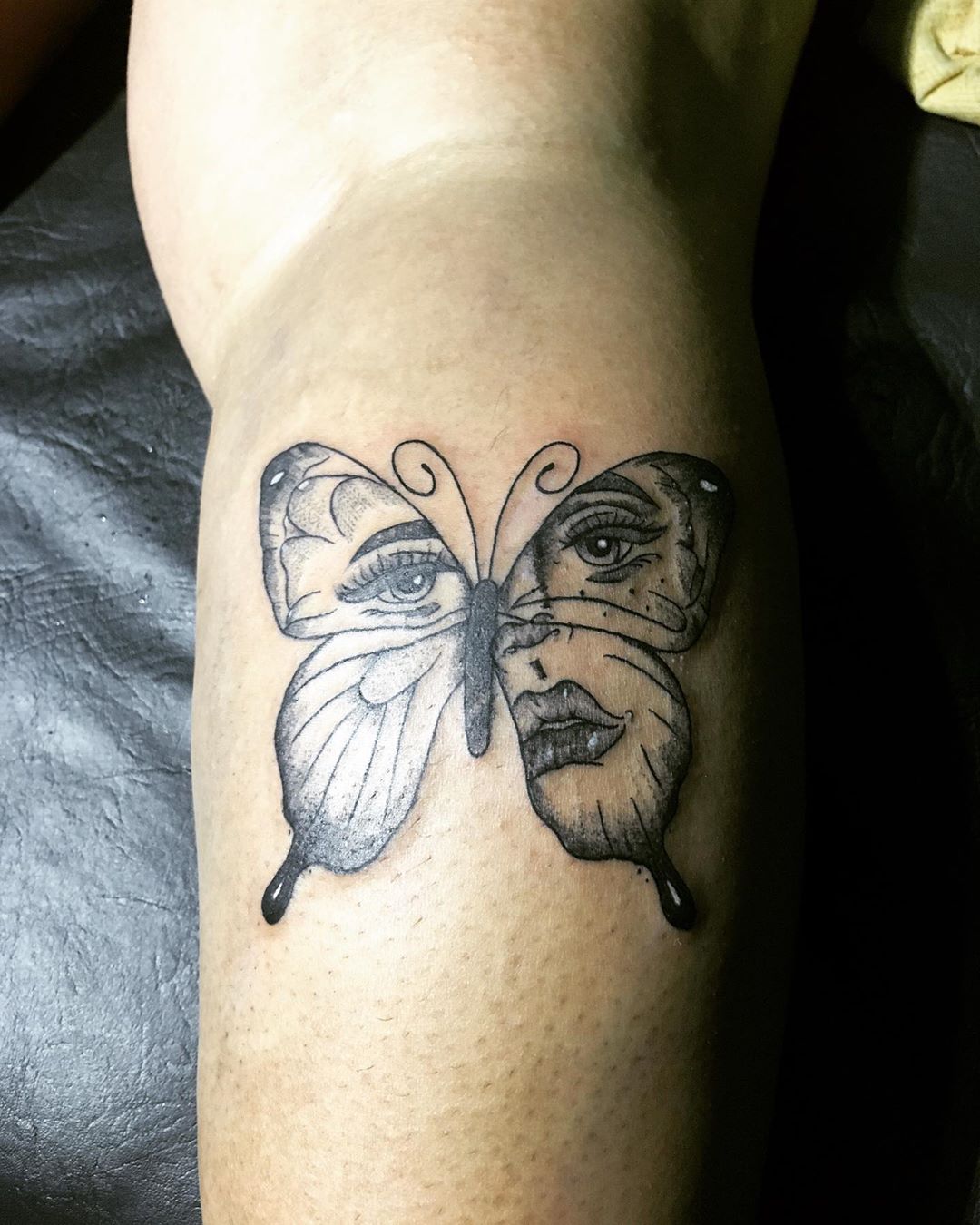 large black and grey tattoo on woman's lower leg of butterfly with woman's face inside wings