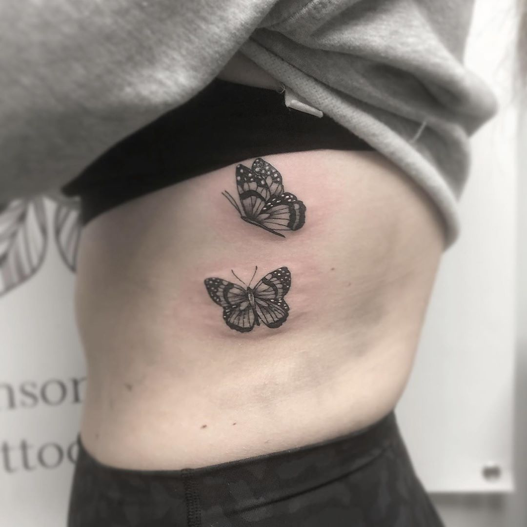 small black and grey tattoo on woman's ribs of two realistic flying butterflies