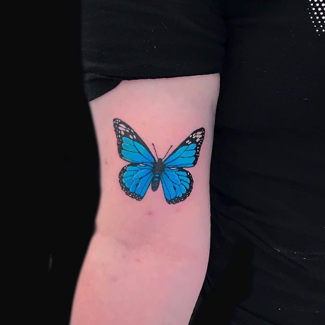 medium-sized color tattoo on woman's upper arm of a realistic blue monarch butterfly