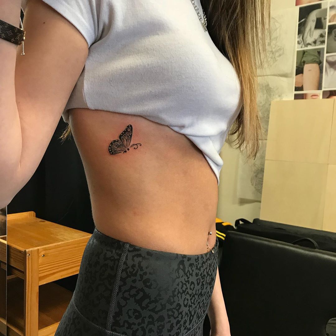 small black and grey tattoo on woman's ribs of realistic flying butterfly