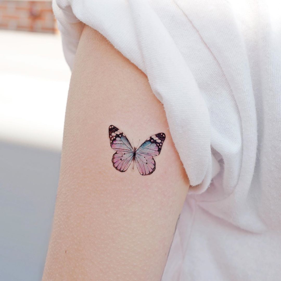 small color tattoo on woman's upper arm of a delicate pink and blue butterfly