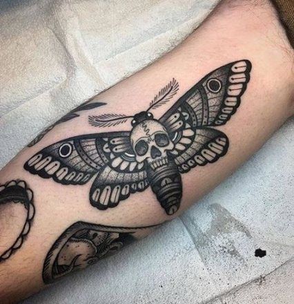 large black and grey tattoo on man's inner upper arm of a realistic moth butterfly with skull in its body